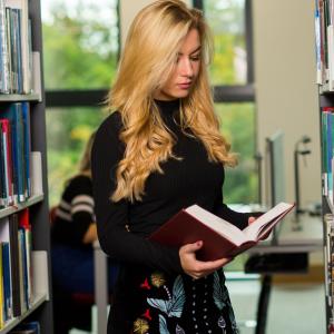Female doctoral student reviewing book between library shelves