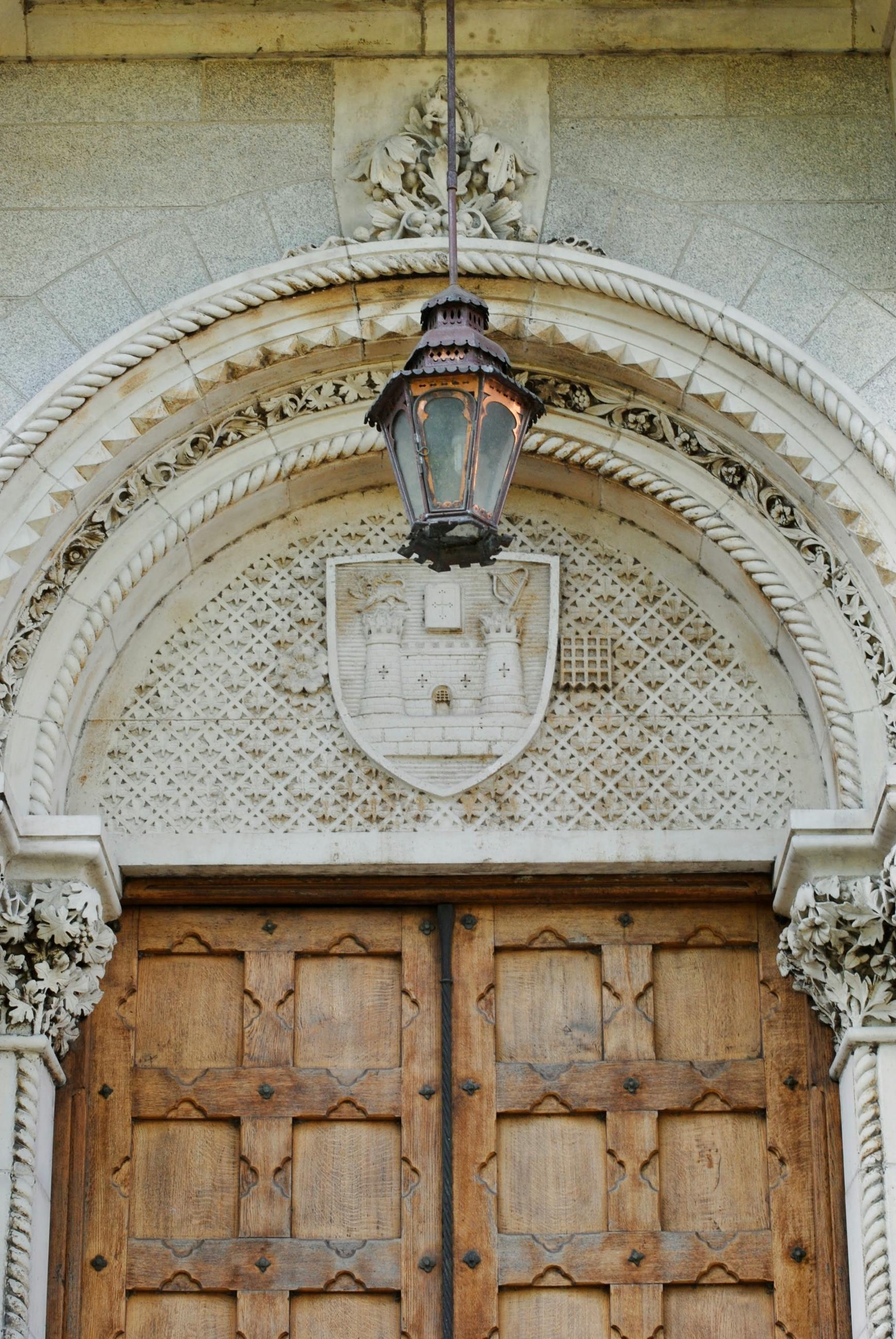 alt="a large wooden door with an old, ornate light fixture above it."