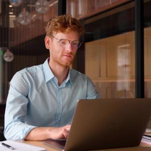 Young professional man, focused, wearing glasses working on laptop, and studying using computer for online seminar webinar at library.